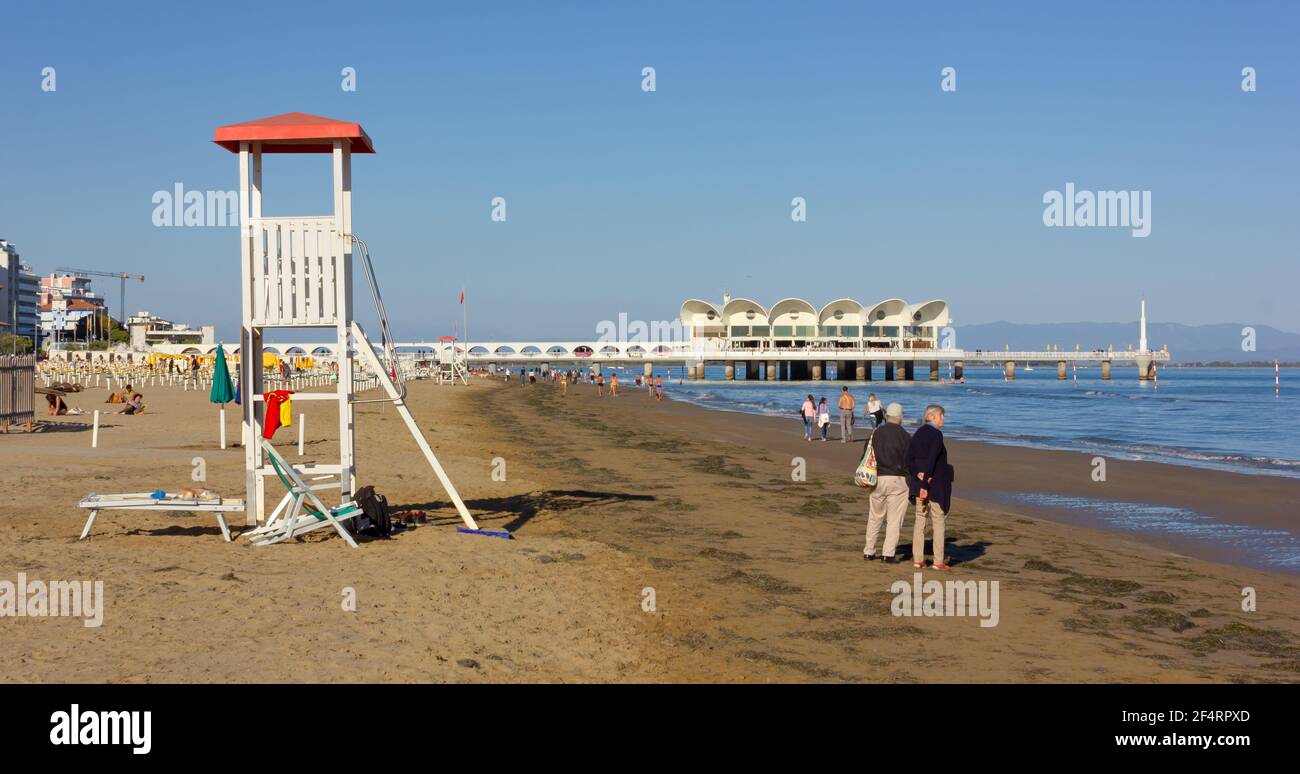 LIGNANO SABBIADORO, Italy - September 30, 2018: People strolling along Sabbiadoro beach, with a lifeguard tower in the foreground Stock Photo
