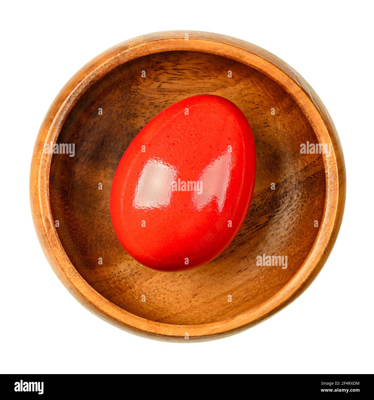 Red dyed Easter egg in a wooden bowl. Hard boiled, colorful dyed chicken egg. Edible Paschal egg, ready to eat, or for an Easter egg hunt. Close-up. Stock Photo