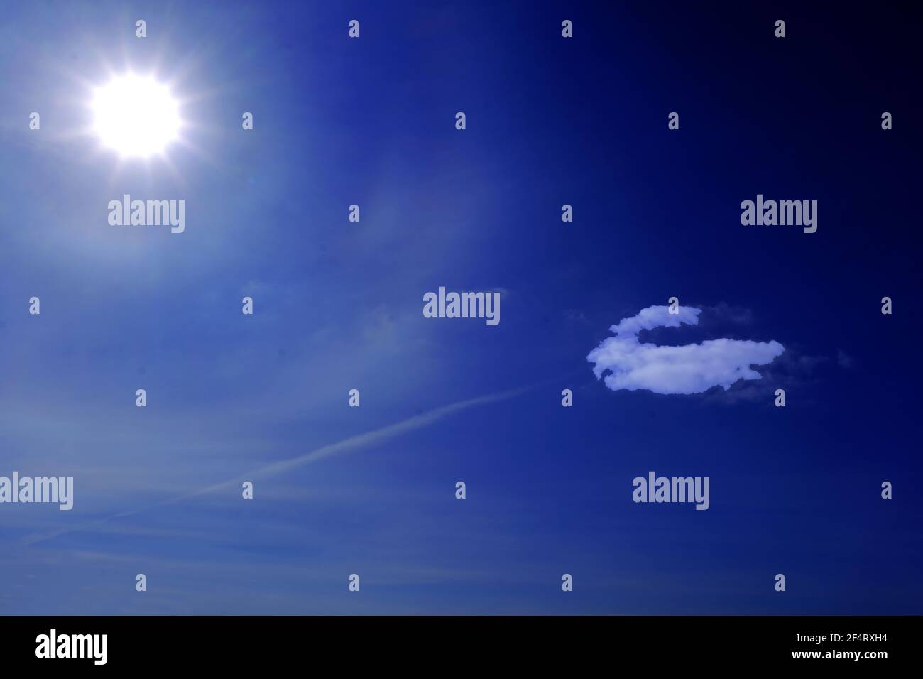 Multi star sun and single white cloud against deep blue sky and contrail Stock Photo