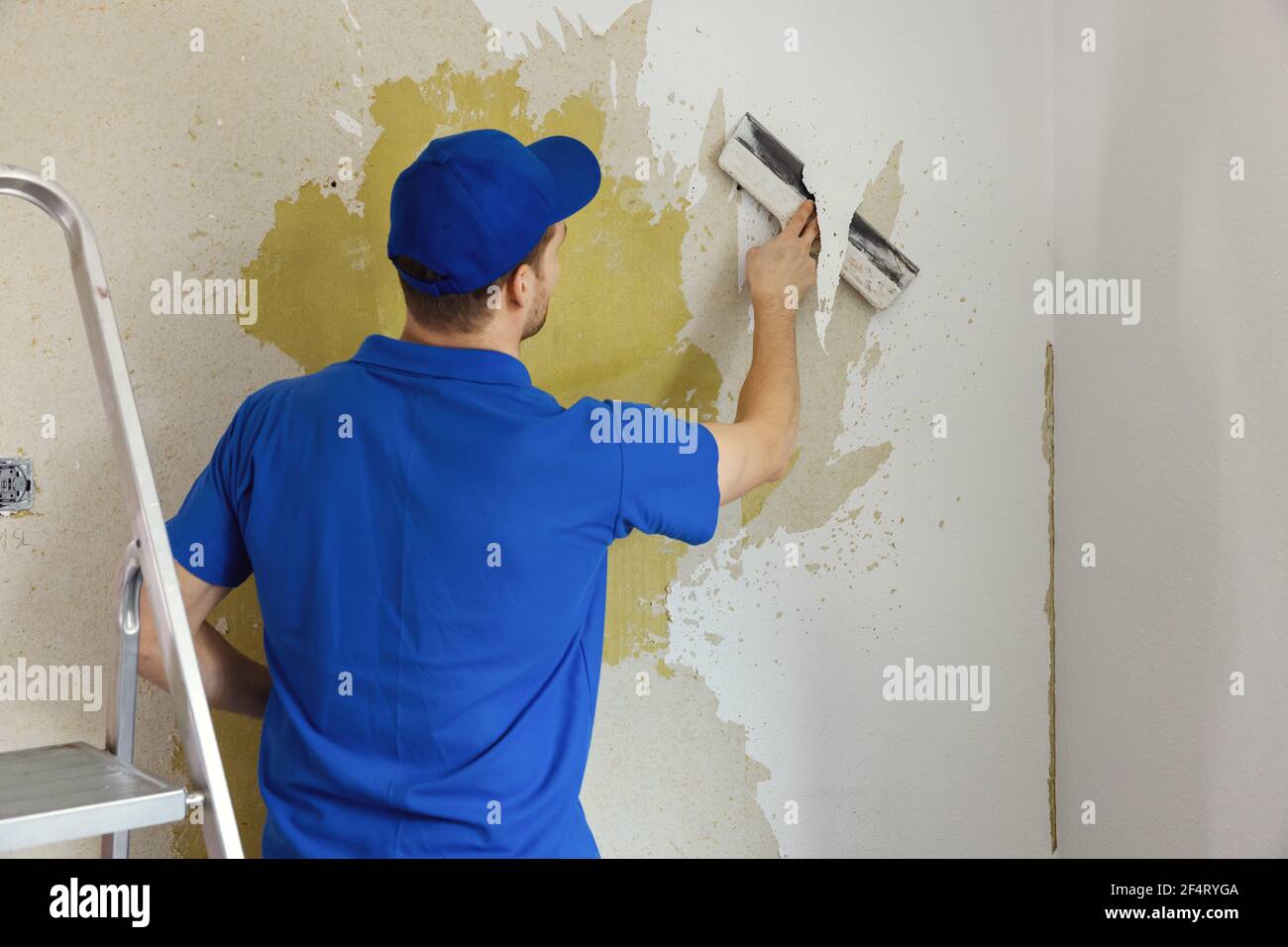 worker removing old painted wallpaper from the wall. house renovation interior renewal Stock Photo