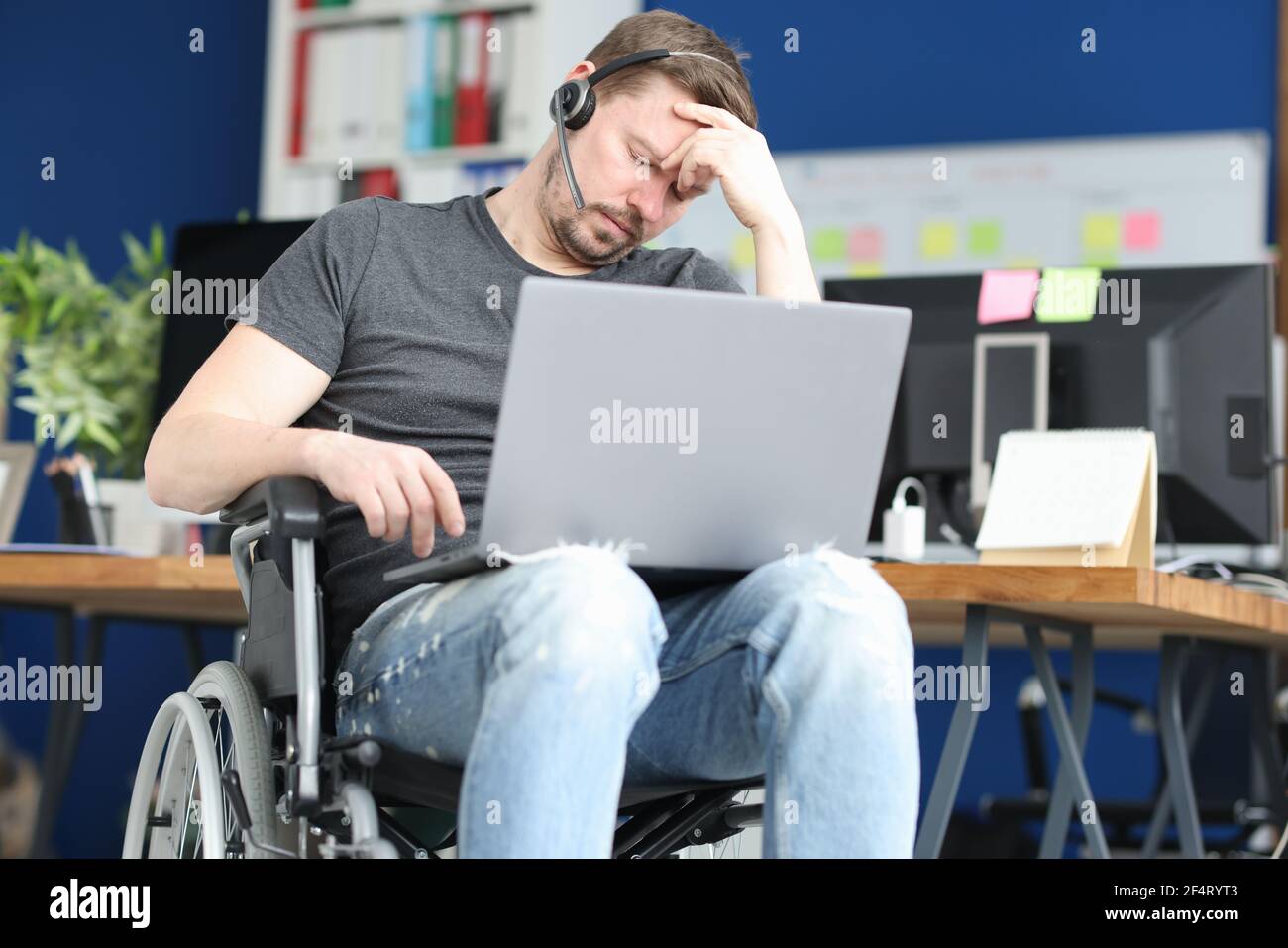 Disabled man sleeping in wheelchair with laptop on his lap Stock Photo