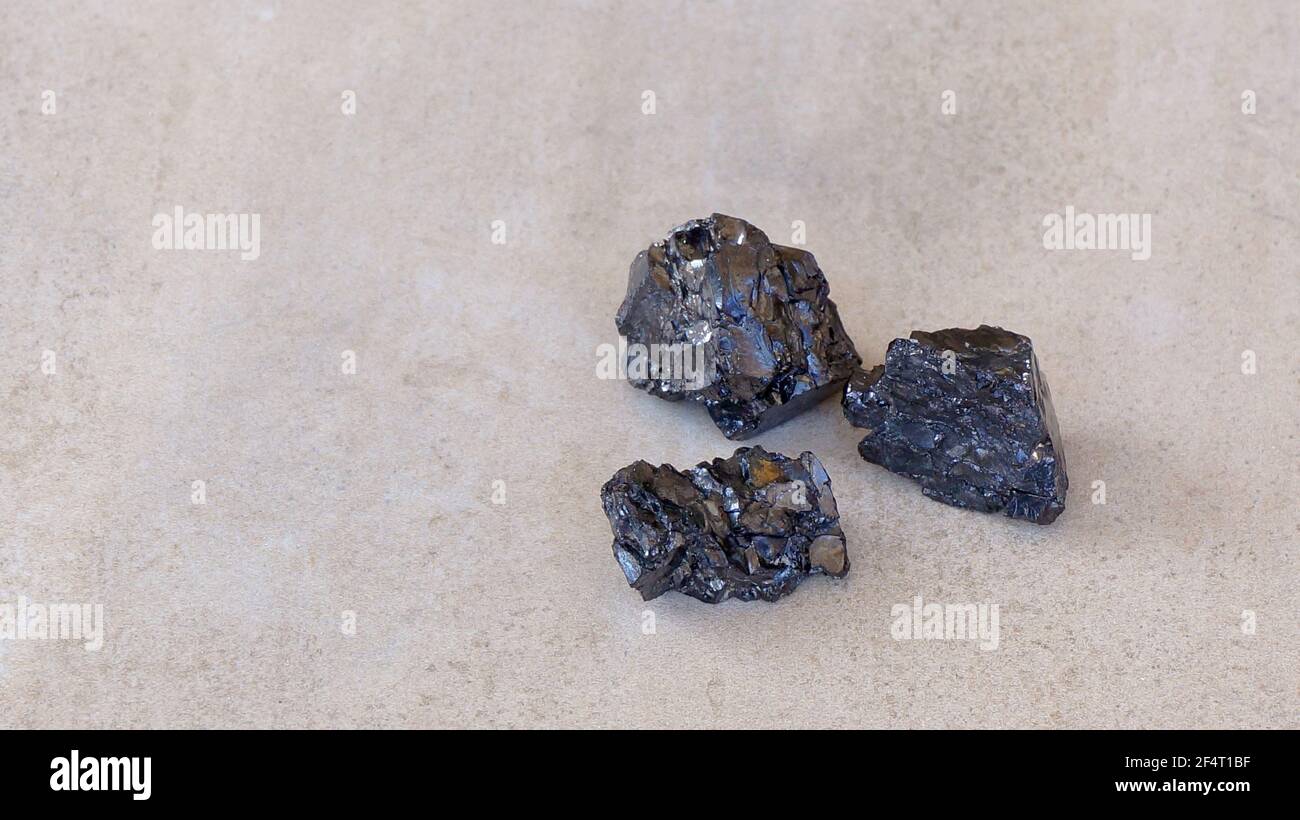Three black shungite mineral stones on light brown background copy paste Stock Photo