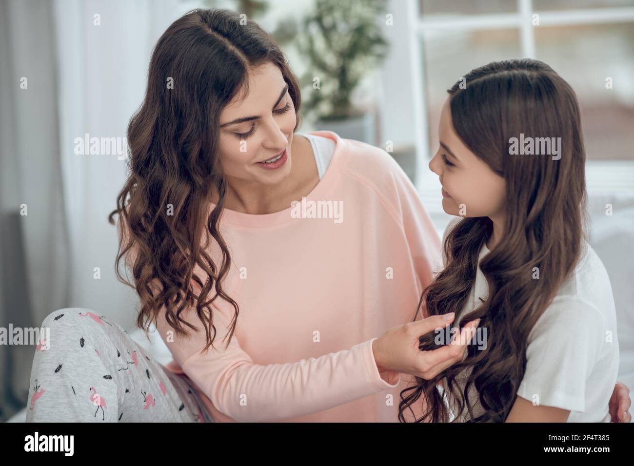 Smiling mom touching daughters long wavy hair Stock Photo