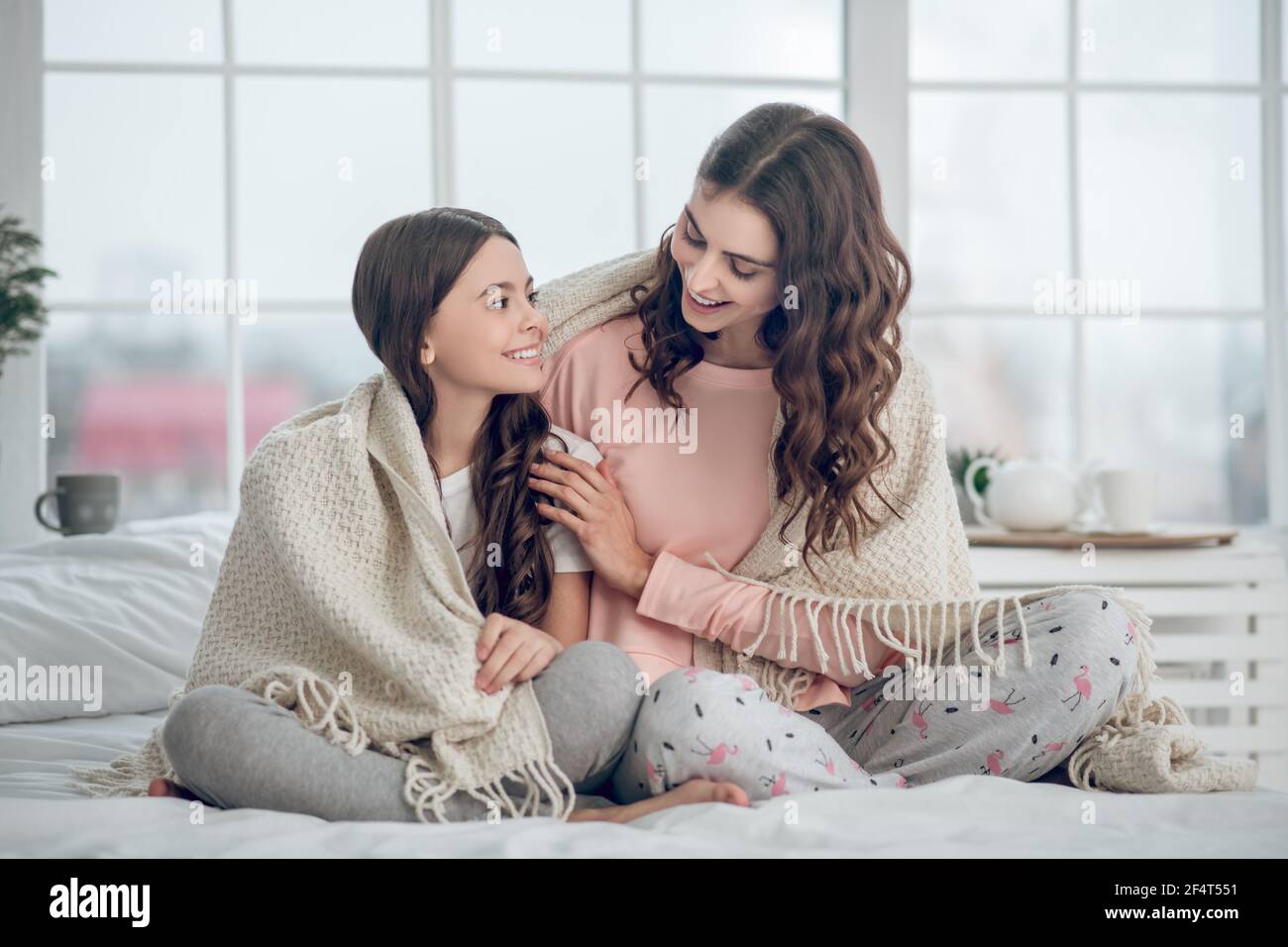 Mom and daughter sitting under blanket on bed Stock Photo
