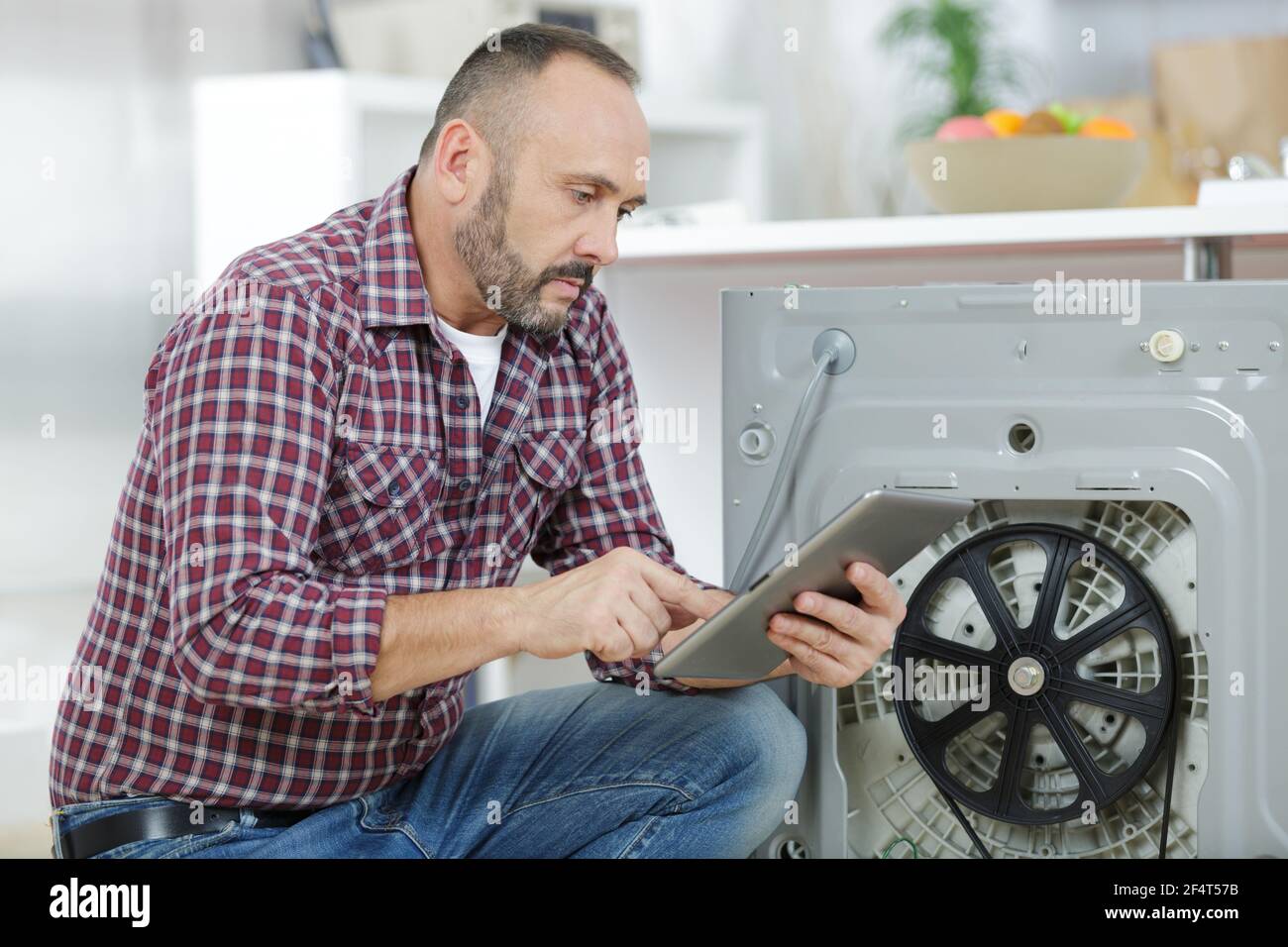 man looking at tablet by broekn down washing machine Stock Photo
