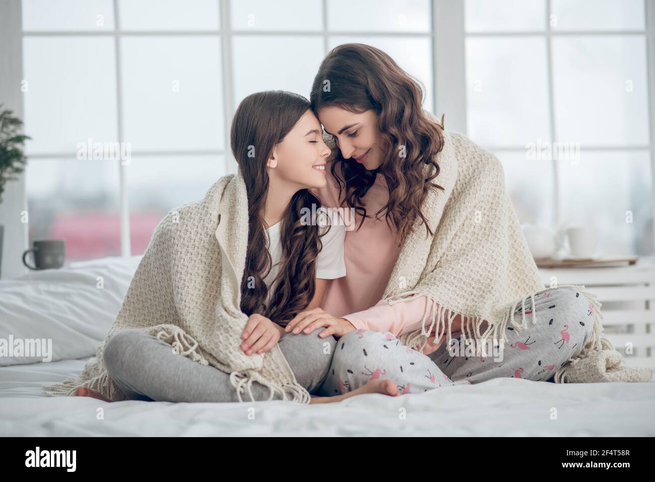 Happy daughter with mom sitting covered blanket Stock Photo