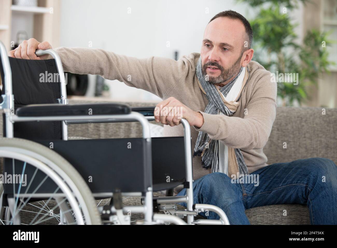 disabled man on sofa preparing to get into wheelchair Stock Photo Alamy