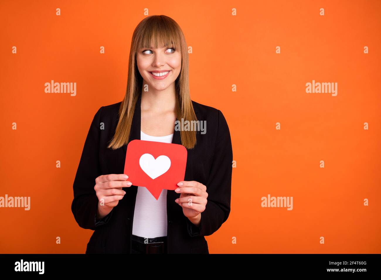 Portrait of lovely trendy minded cheerful girl holding in hands paper red card web looking aside copy space isolated over bright orange color Stock Photo