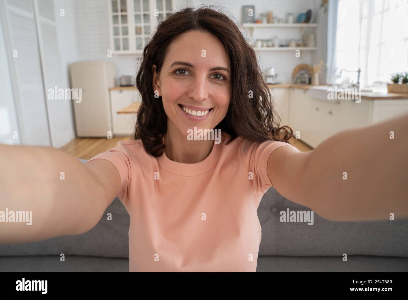 Happy woman recording new content to vlog stretching arm to camera, photographing herself at home.  Stock Photo