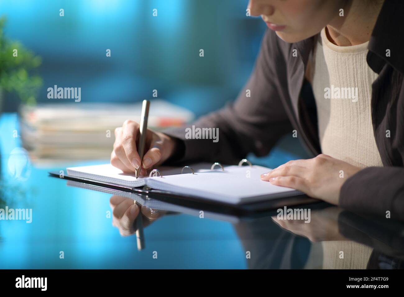 Close up of a woman hands taking notes in a ring binder notebook on a desk in the night at home Stock Photo