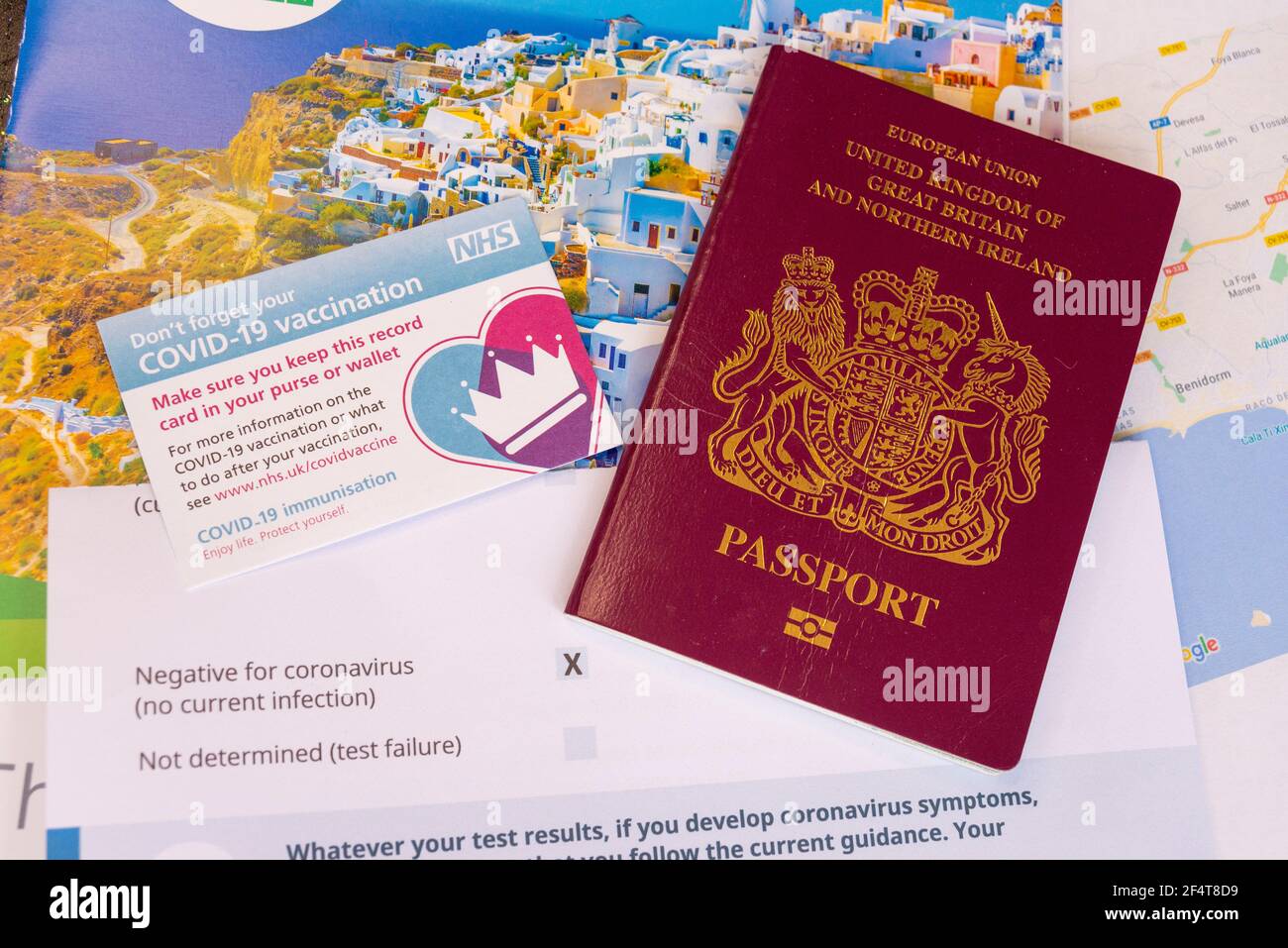 UK COVID 19 vaccine travel passport concept, with NHS vaccination record card, UK EU passport, negative test result, holiday brochure and Spain map Stock Photo