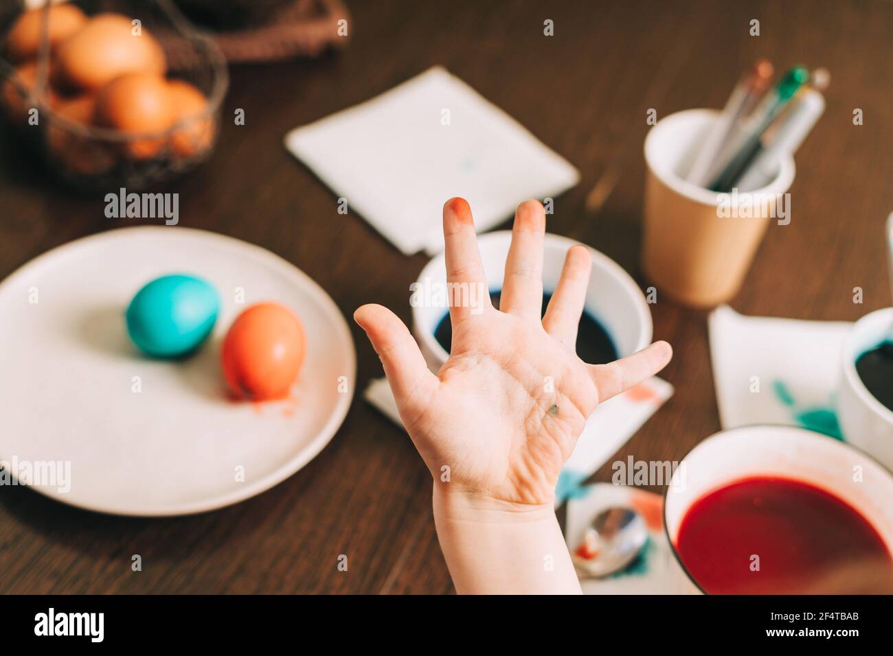Easter day. Dirty hand of Kid boy painting eggs on wooden background. Child sitting in a kitchen. Preparing for Easter, creative homemade decoration Stock Photo