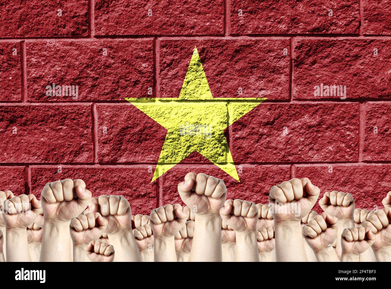 Raised fists against the background of the depicted flag of Vietnam on a brick wall, a concept of strength and unity. Stock Photo