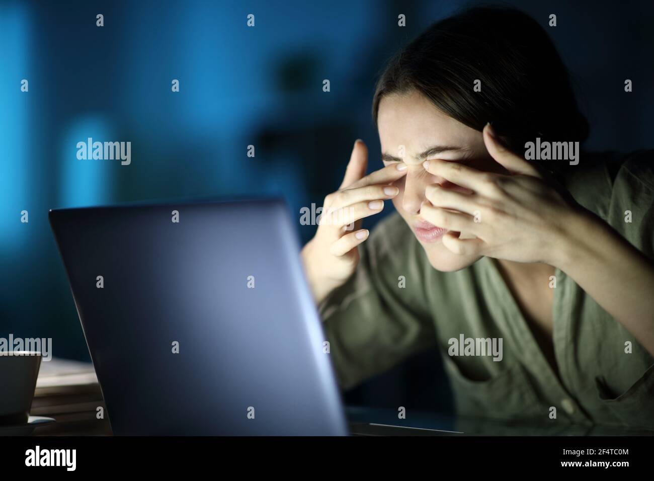 Fatigued woman with eyestrain scratching eyes using laptop late hours in the night at home Stock Photo