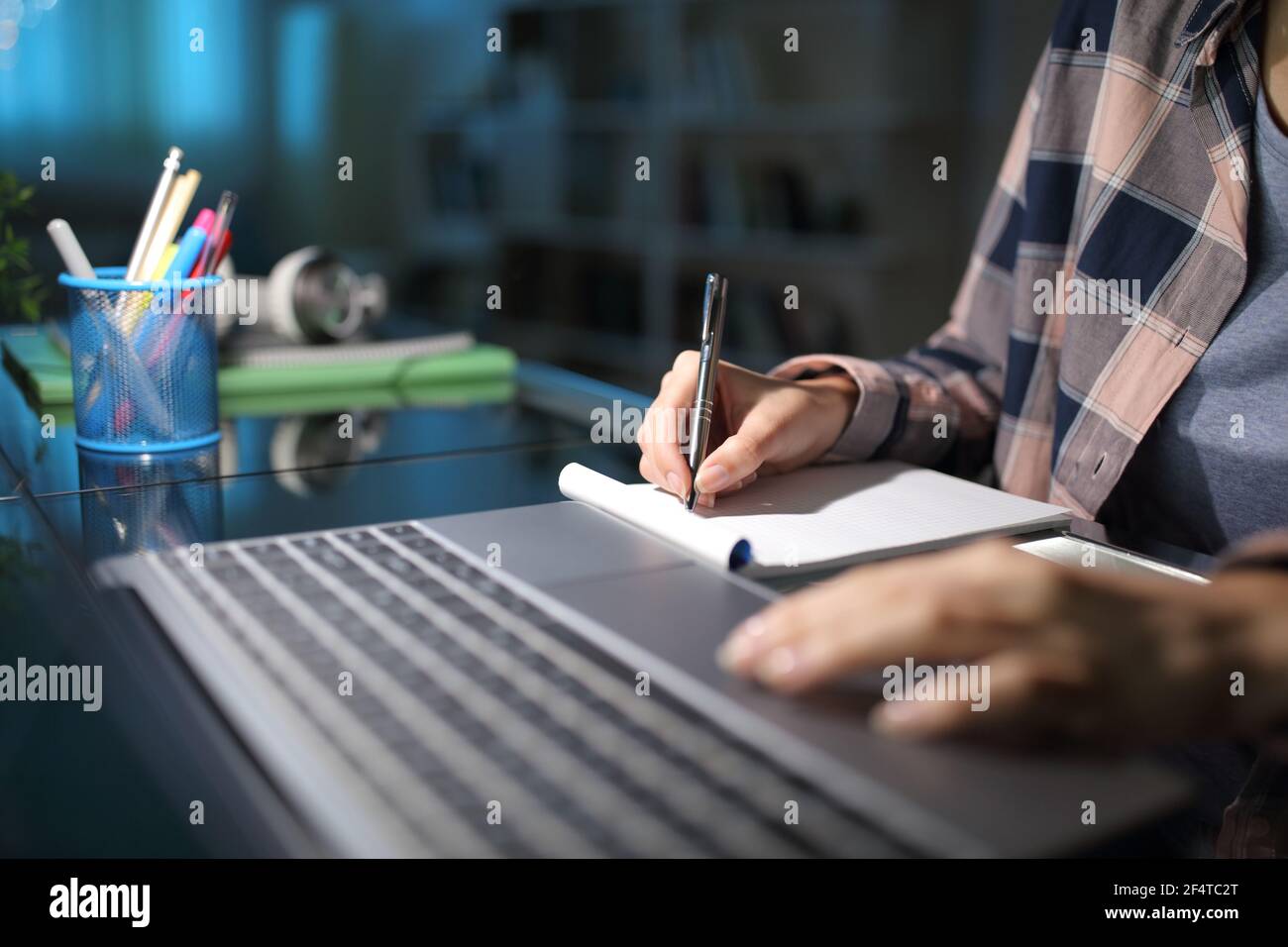 Close up of a student hand taking notes checking laptop in the night at home Stock Photo