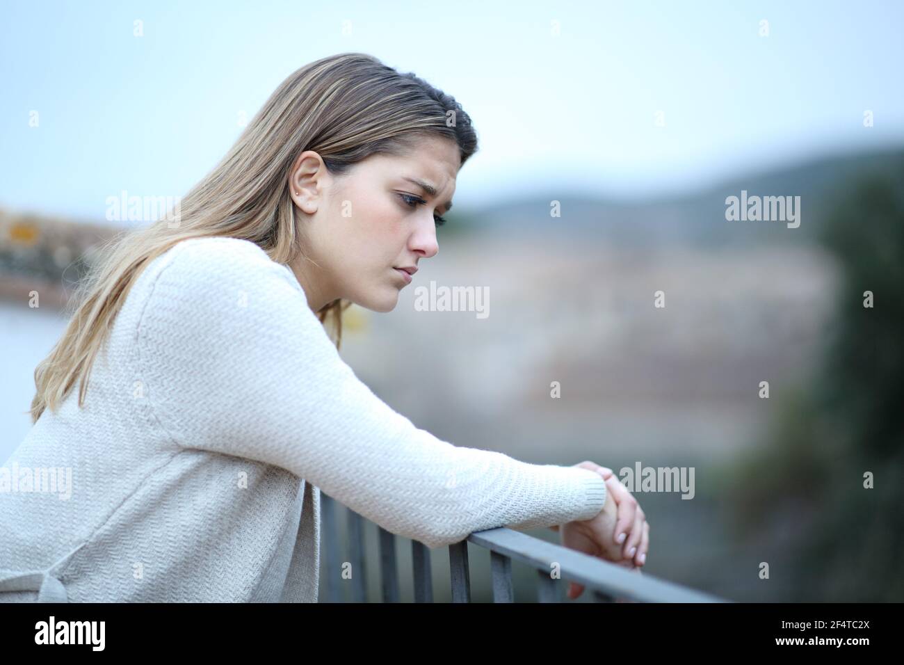 Sad woman looking down in a house balcony complaining alone in a town Stock Photo