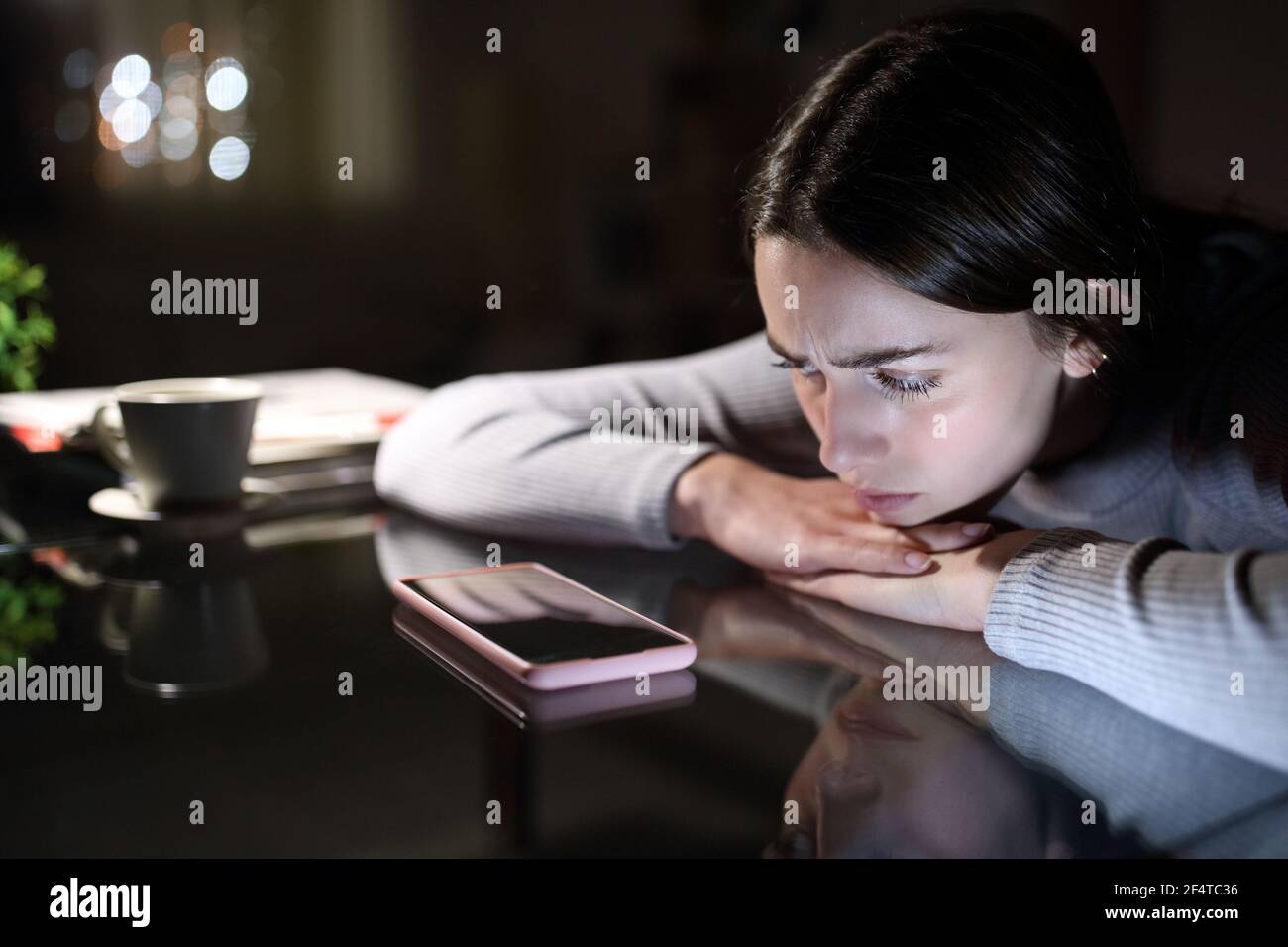 Sad woman waiting for a mobile phone call looking it in the night at home Stock Photo