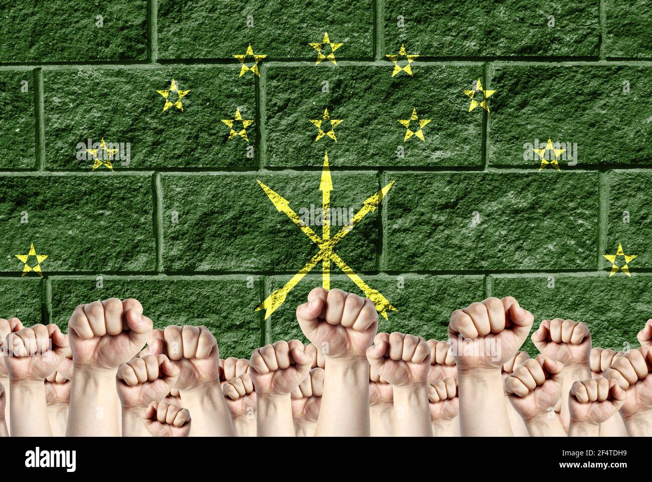 Raised fists against the background of the depicted flag of Adygea on a brick wall, a concept of strength and unity. Stock Photo