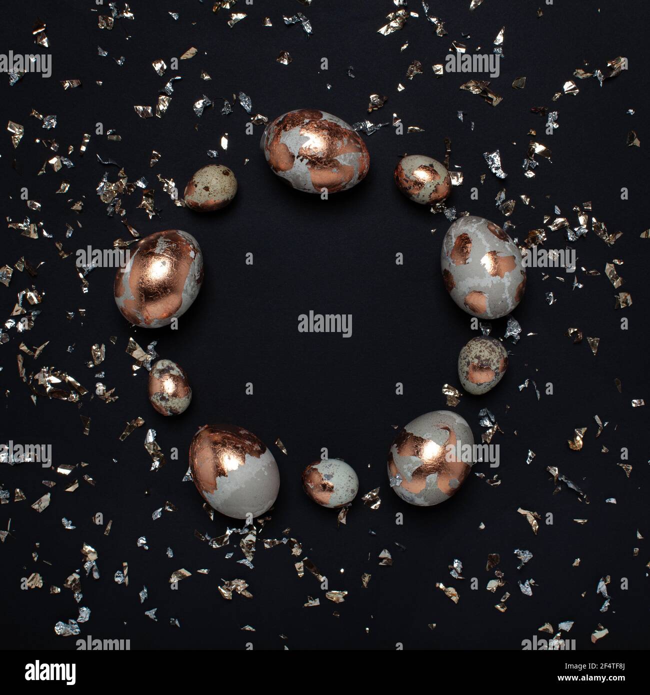Gilded eggs and shiny confetti on a black background. Stock Photo