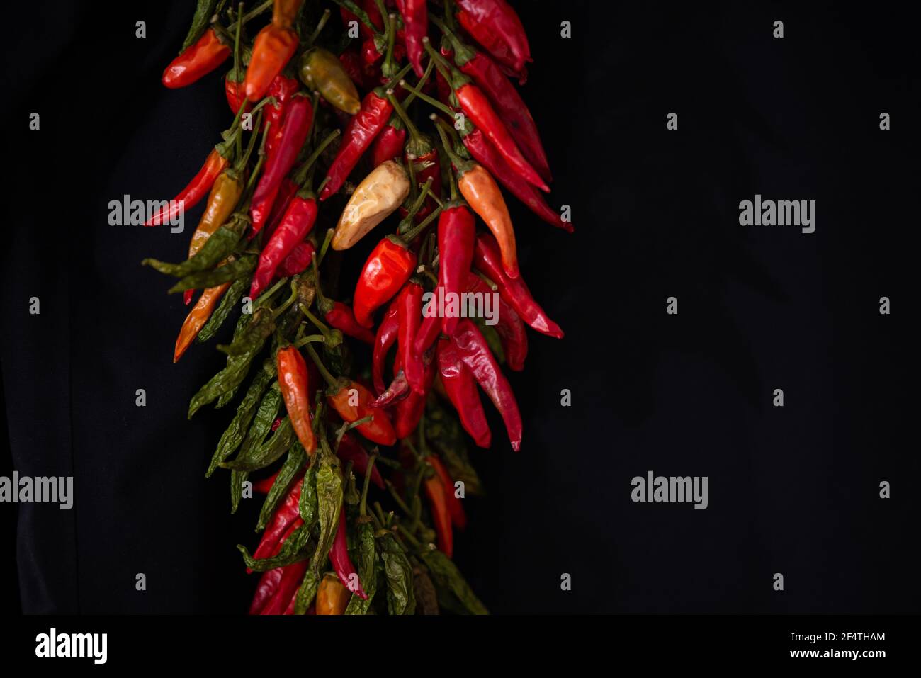 Bunch of red hot chili peppers hanging and drying on a rope on a black ...