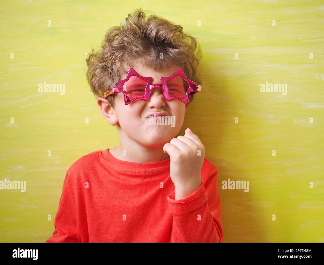 Fun kid in eyeglasses in shape of star makes funny face. Yellow background. Stock Photo