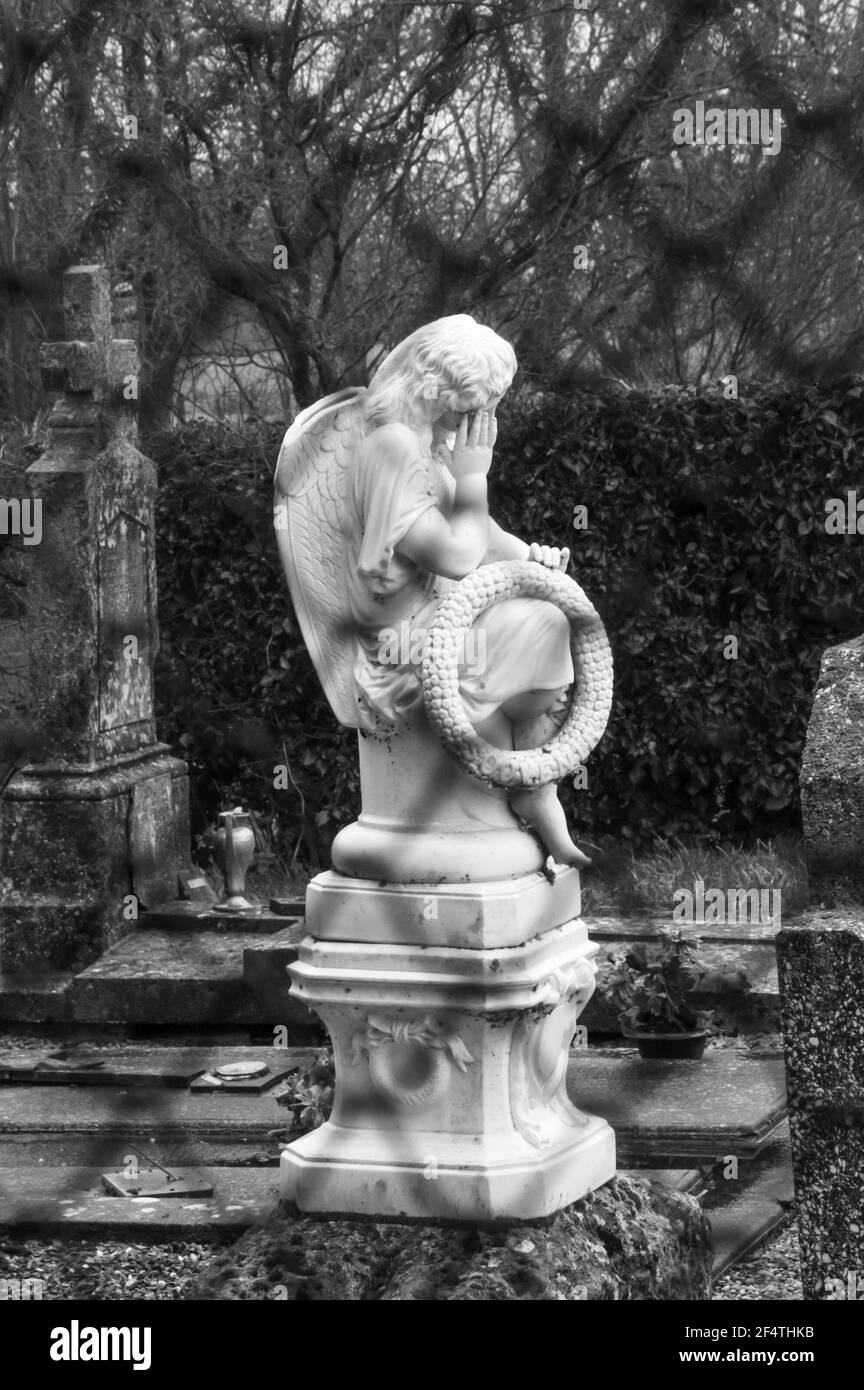 Old cemetery with mourning angel on the tomb holding wreath with word