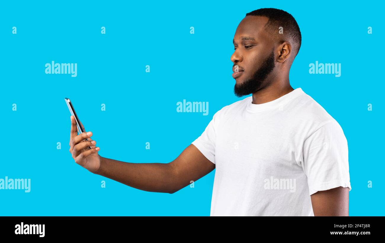 Black Man Scanning Face Using Phone Standing Over Blue Background Stock Photo