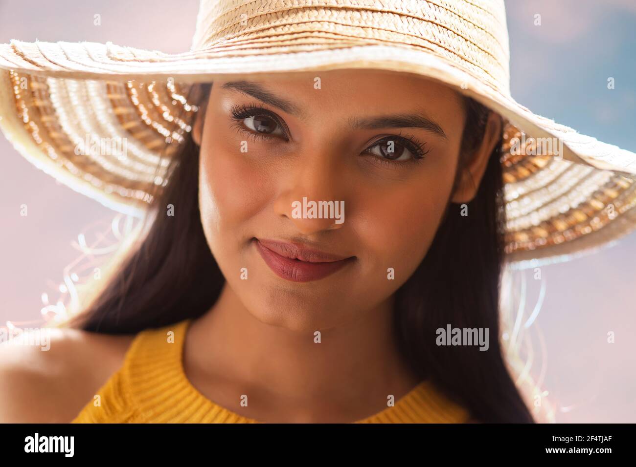 CLOSE SHOT OF A YOUNG WOMAN WEARING SUMMER HAT AND LOOKING AT CAMERA Stock Photo