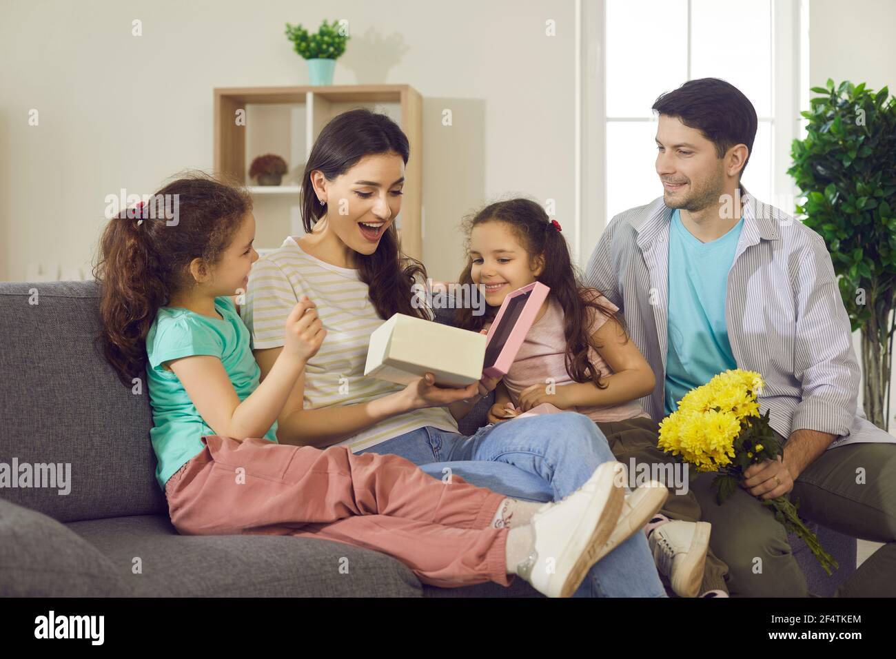 Pleasant surprised mom with happy expression opening gift box from kids Stock Photo