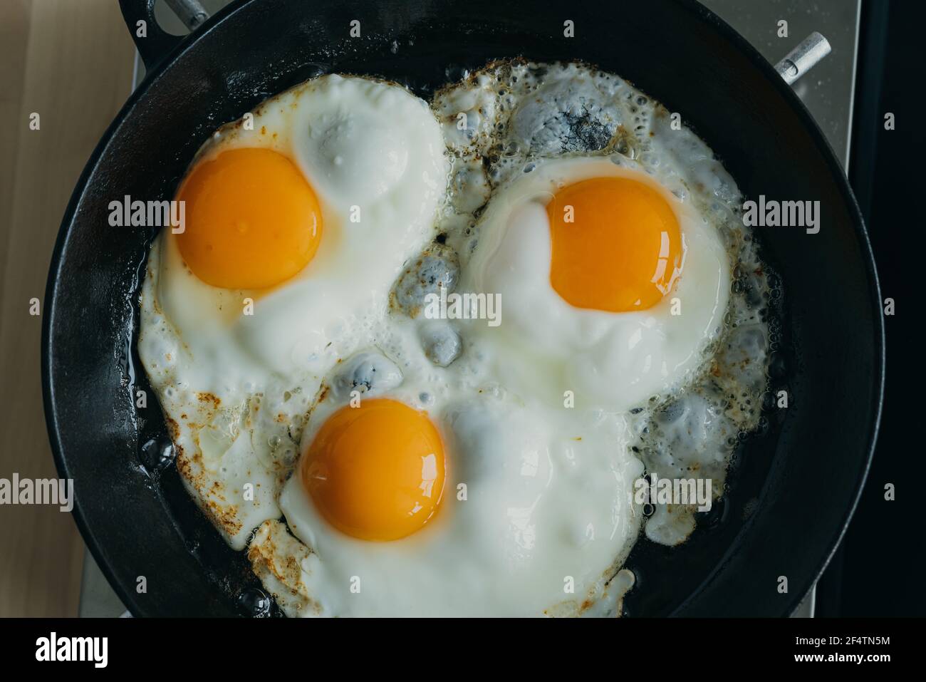 Keto meal eggs frying on hot cast iron frying pan, three fried yellow