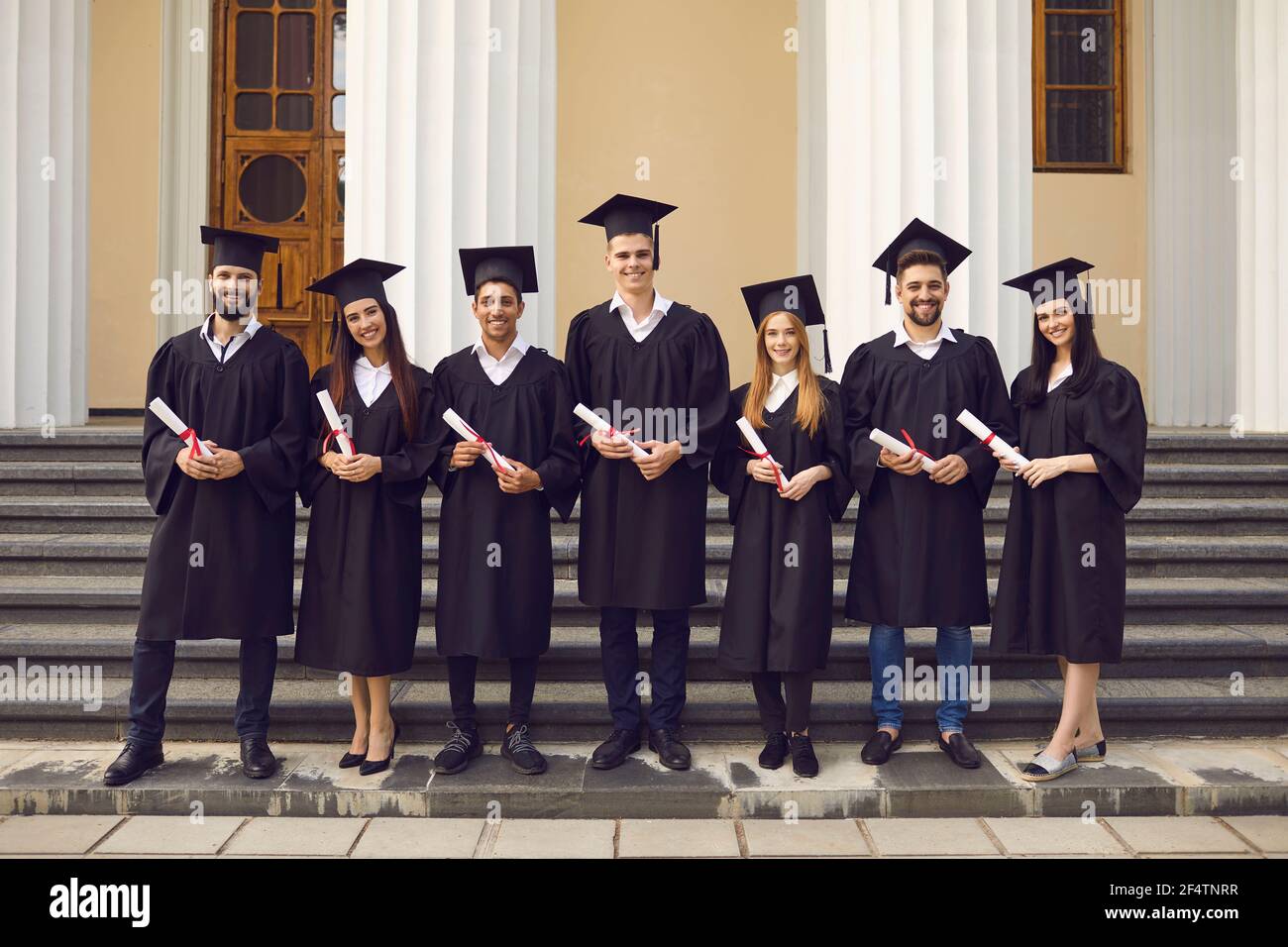 Group of graduates in academic dresses posing with diplomas against the