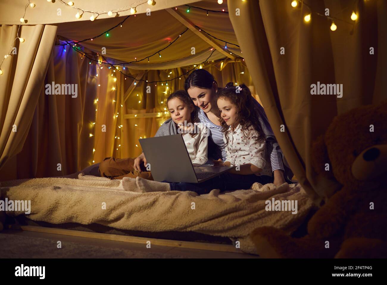 Mother with preschool daughters watching movie on laptop in kids tent at home Stock Photo