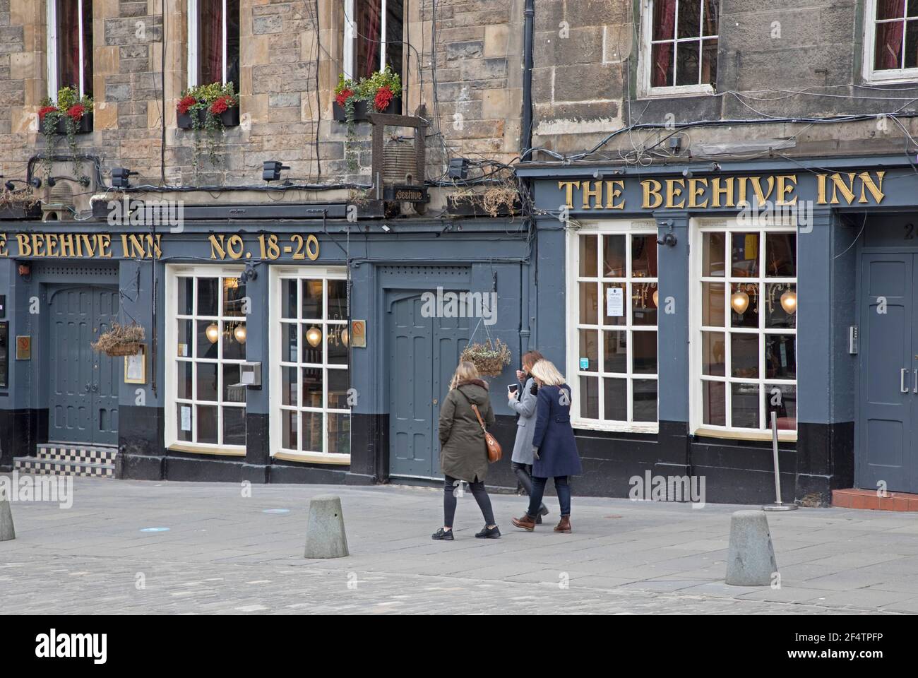 Edinburgh city centre, Scotland, UK. 23rd March 2021. 'National Day of Reflection' on the Anniversary of the UK's first Covid-19 lockdown. Pictured: Three women pass the closed Beehive Inn in the Grassmarket. Credit: Arch White/ Alamy Live News. Stock Photo