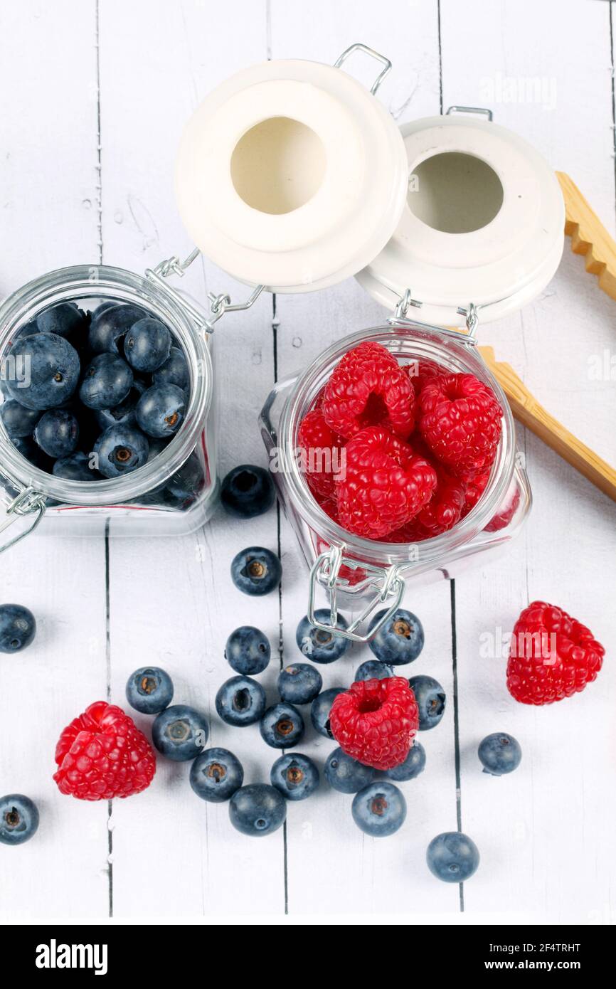 Vertical shot of raspberries and blueberries in jars and a wooden ...