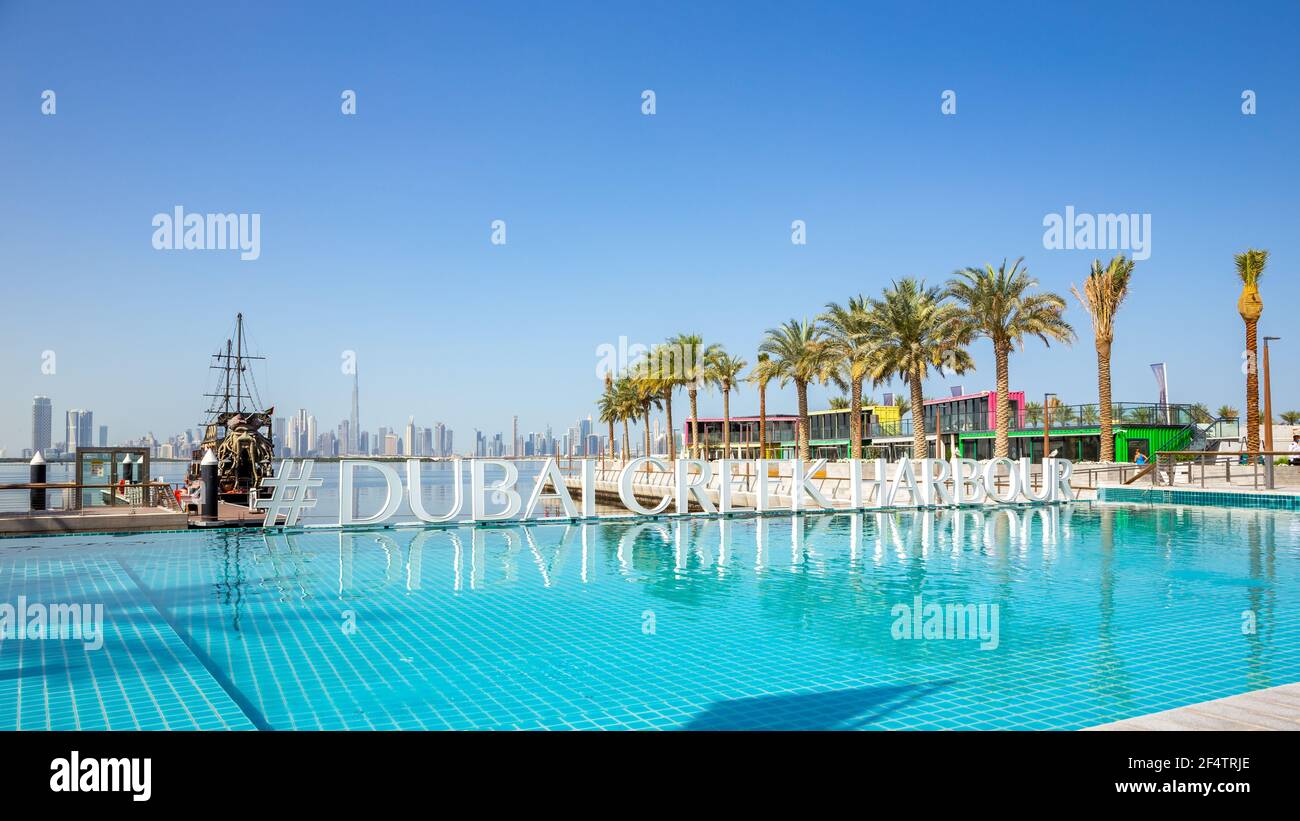 Dubai, UAE, 22.02.2021. Dubai Creek Harbour sign by turquoise water infinity pool with rows of palm trees, Black Pearl Pirate Ship and Dubai Downtown Stock Photo