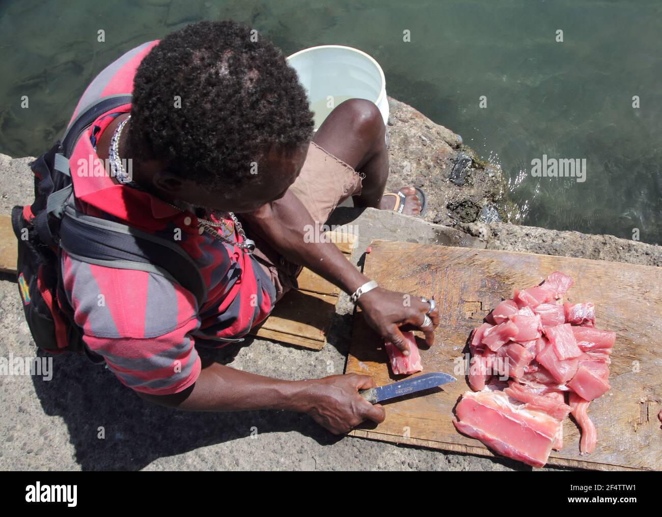 St George's Grenada The Carnage Man Cutting up Freshly Caught Fish using Knife at Water's Edge Stock Photo