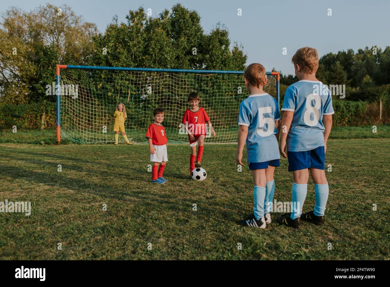 Children playing amateur football. Cheerful kids in teams wearing soccer dresses having fun playing soccer in field at sunset. Stock Photo