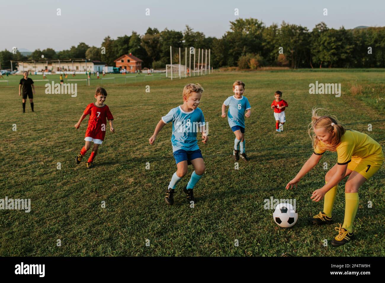 Children playing amateur soccer. Cheerful boys chasing football ball outside on pitch at sunset. Stock Photo