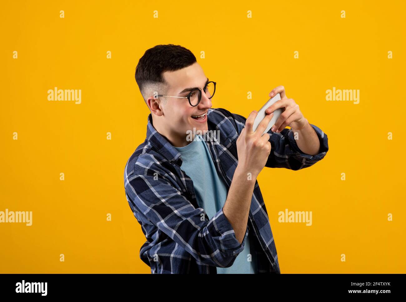 Online gaming concept. Portrait of positive young guy playing video games on smartphone over orange studio background Stock Photo