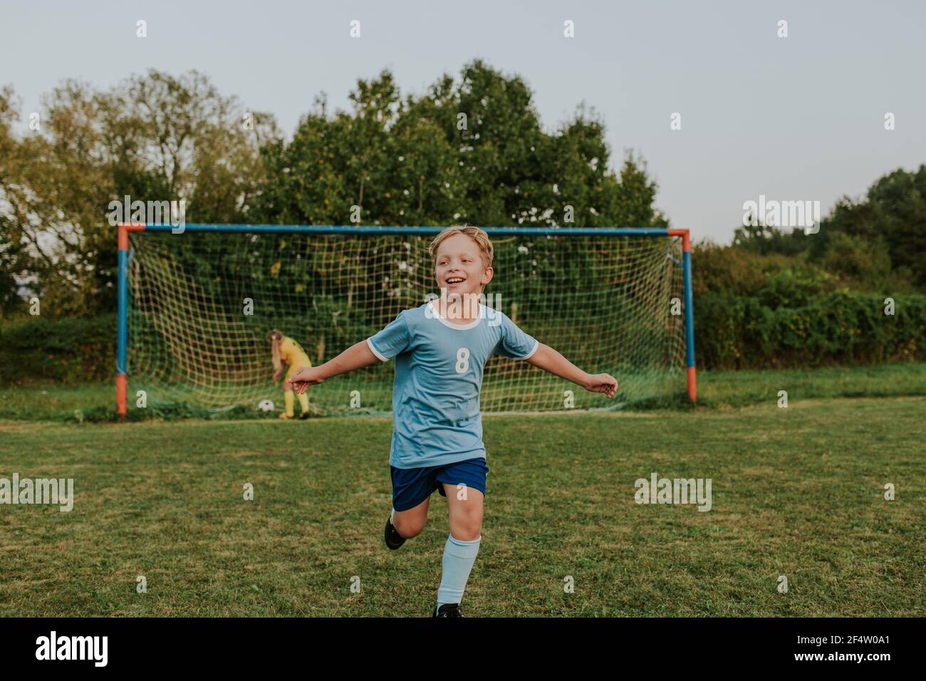 Children playing football outside on pitch. Full length of happy boy scoring goal during amateur soccer game. Stock Photo