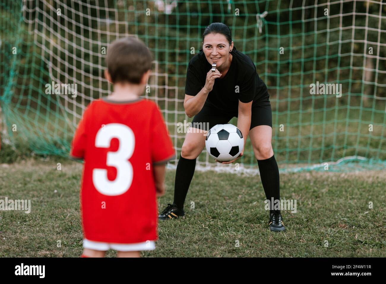 Female referee throwing ball to toddler boy on football field. Woman in