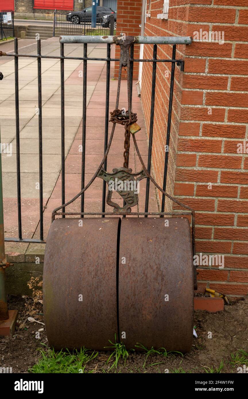 A old heavy garden roller chained to a metal fence Stock Photo
