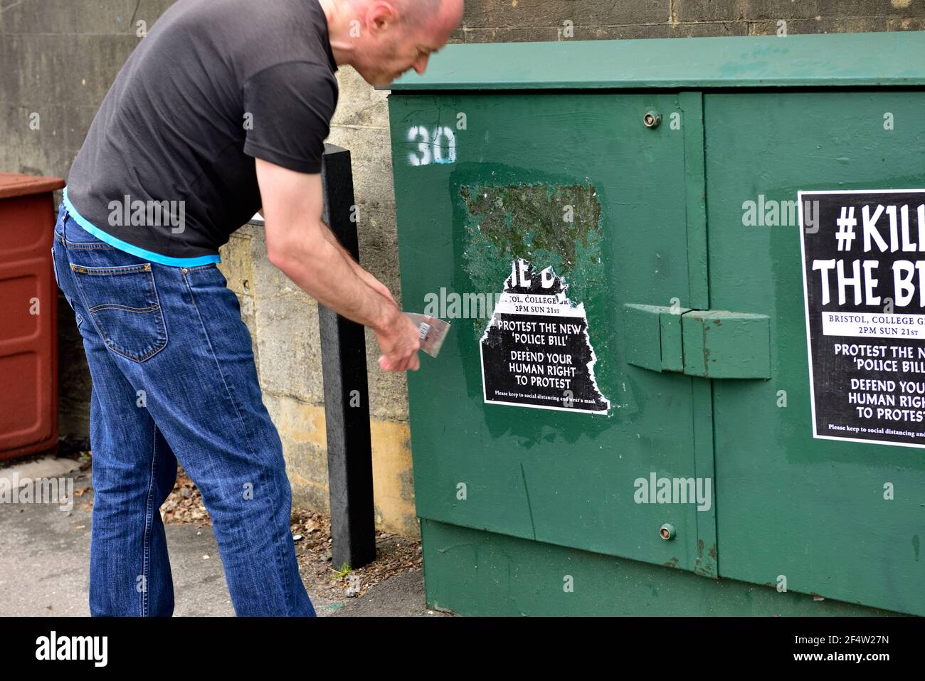 Man busy scrapping off  “Kill the Bill” poster stuck on box by protesters in violent disorder in Bristol city centre in next days clean up Stock Photo