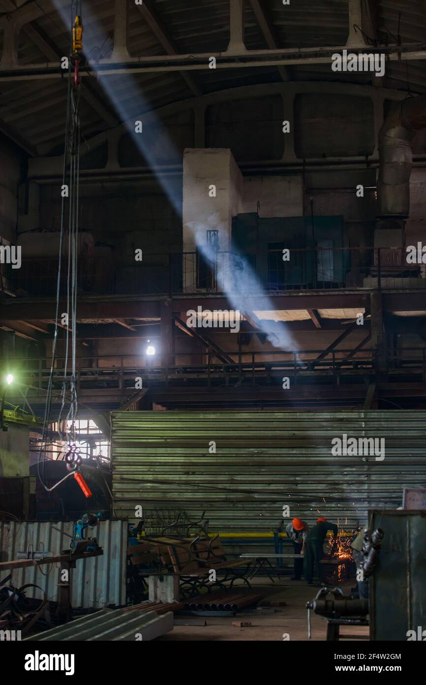 Workshop of reinforce concrete plant. Welder workers, smoke and sunbeam. Dark tones. Stock Photo