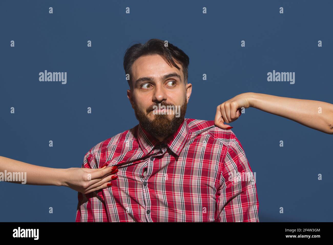 Female hands rumple young bearded handsome man on blue background Stock Photo