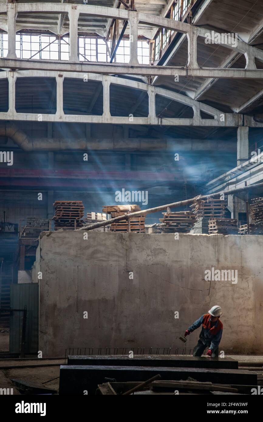 Workshop of reinforce concrete plant. Worker with brush making marks. Smoke and sunbeam. Dark tones. Stock Photo