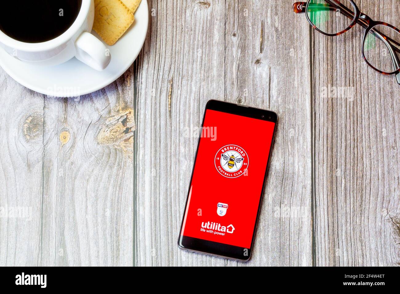 A mobile phone or cell phone laid on a wooden table with the Brentford football Club app open on screen Stock Photo