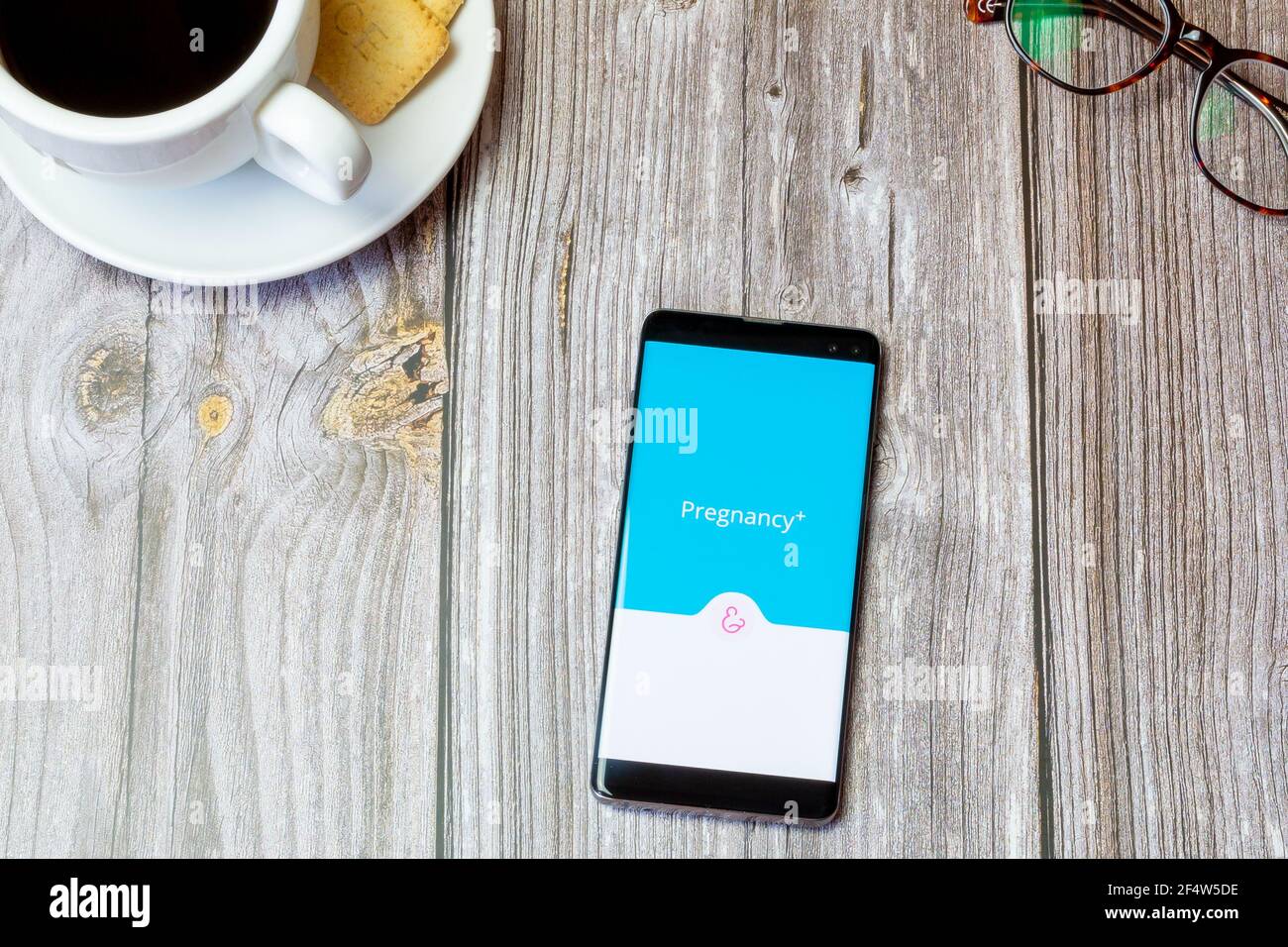 A mobile phone or cell phone laid on a wooden table with the Pregnancy plus app open on screen Stock Photo
