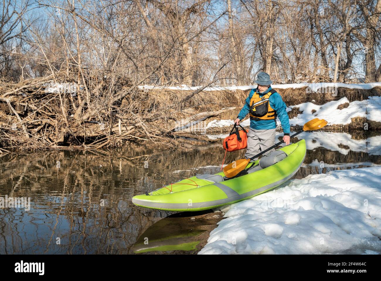 senior male paddler is launching an inflatable whitewater kayak on a ...