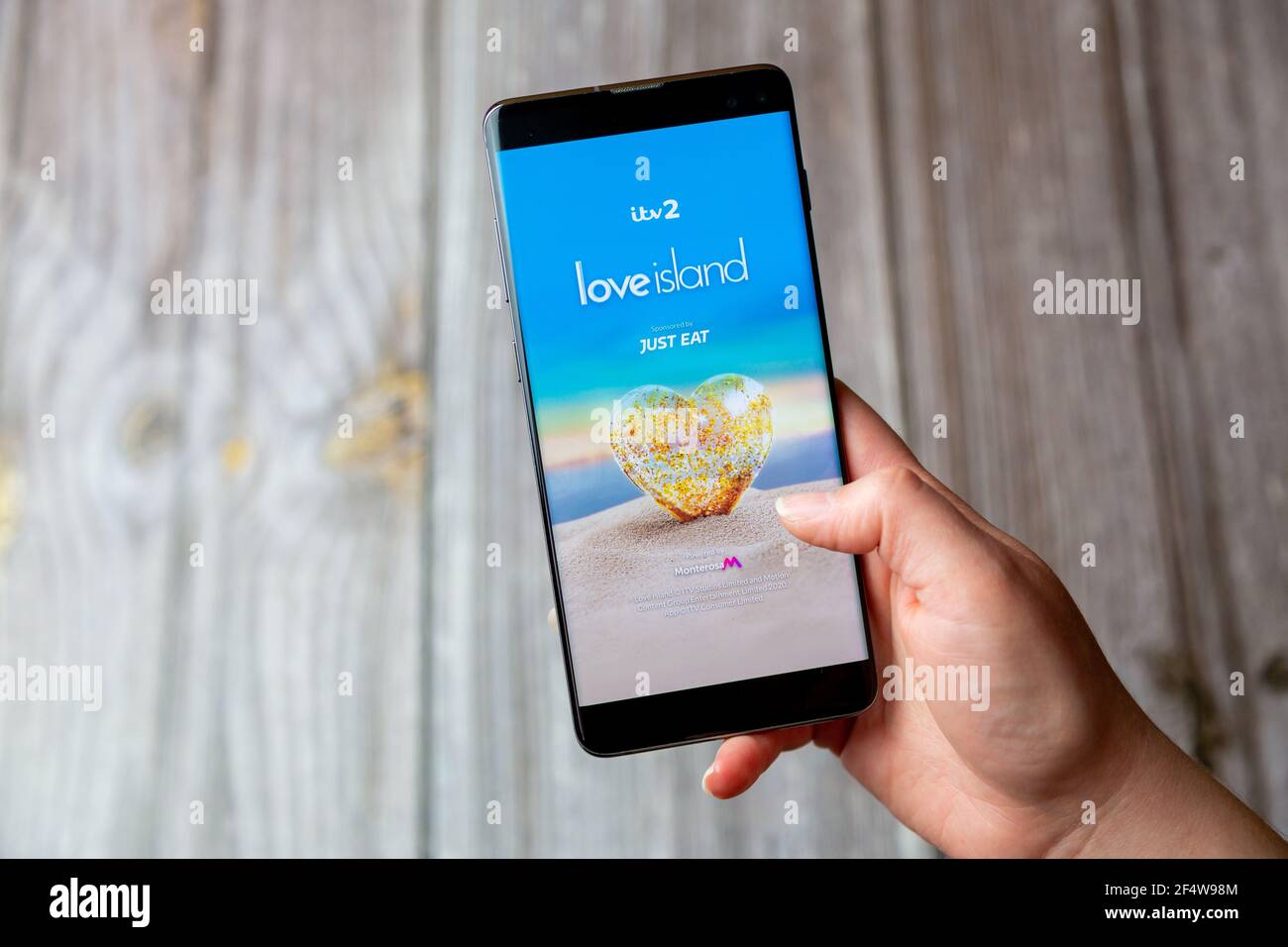 A mobile phone or cell phone being held in a hand with the Love Island app open on screen Stock Photo